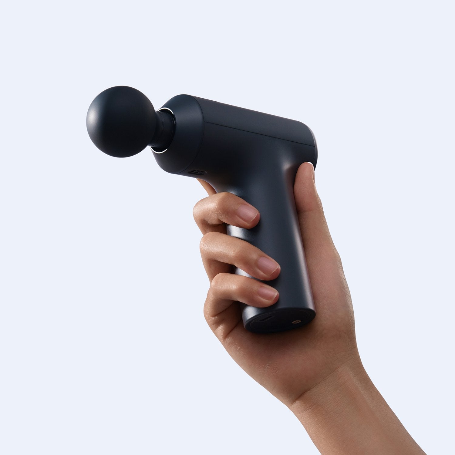 Hand holding a black massage gun against a light gray background