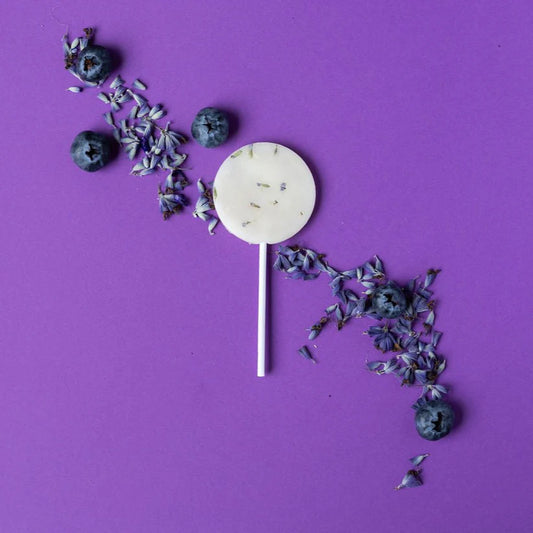 White lollipop with blueberries and lavender on a purple background