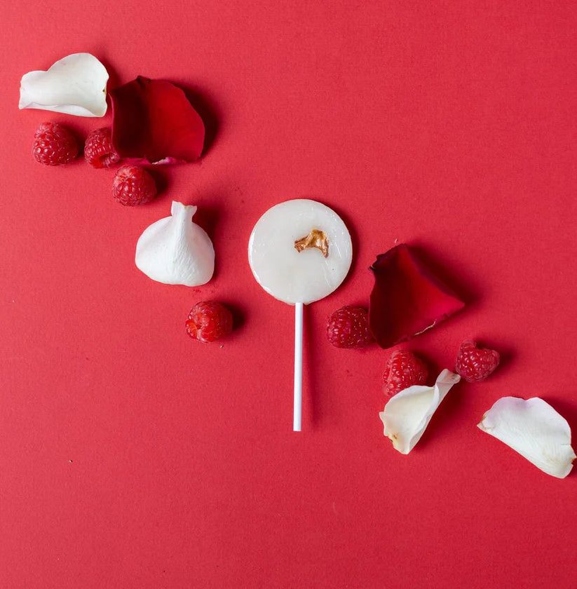 White lollipop with a ring on a red background with raspberries and flower petals.