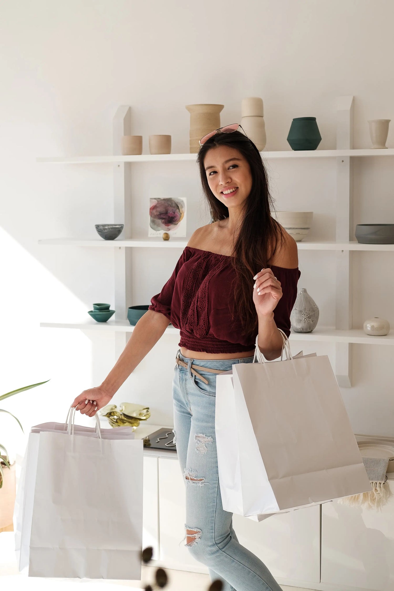 Woman holding shopping bags in a room with shelves displaying various items
